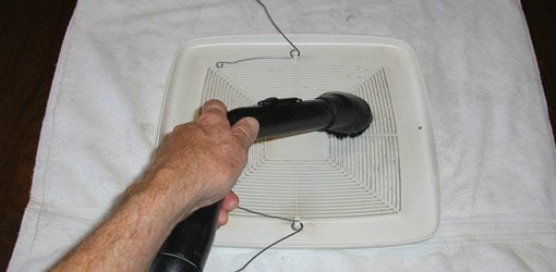 Usando un cepillo para polvo en una aspiradora para limpiar la tapa del ventilador de ventilación.
