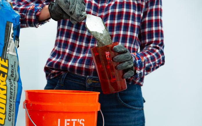 Una mano enguantada usa una paleta de albañilería para verter la mezcla de concreto en un vaso de plástico